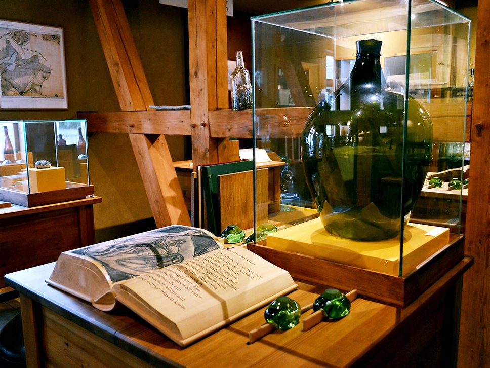 Blick in einen Museumsraum, ein aufgeschlagenes Buch, dahinter ein altes Glasgefäß.
