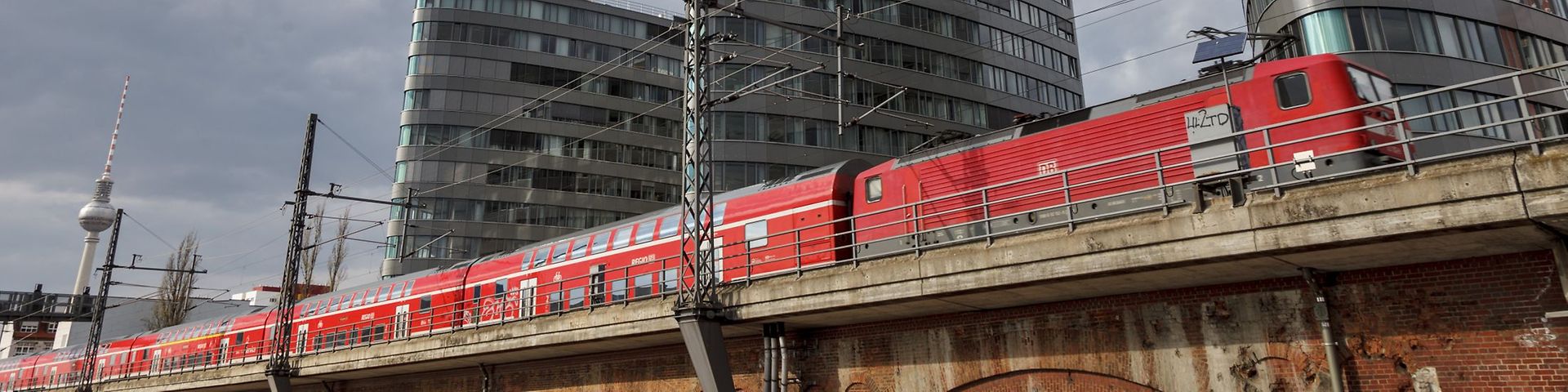 Ein roter Regionalzug führt durch Berlin, im Hintergrund ist der Fernsehturm zu sehen.