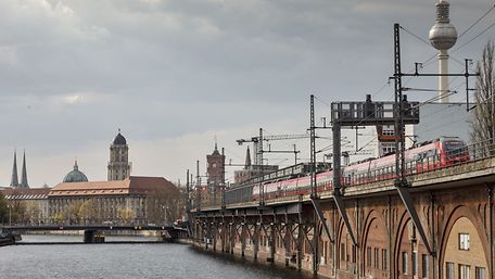 Ein roter Regionalzug fährt entlang der Berliner Stadtbahn, im Hintergrund erkennt man den Fernsehturm.