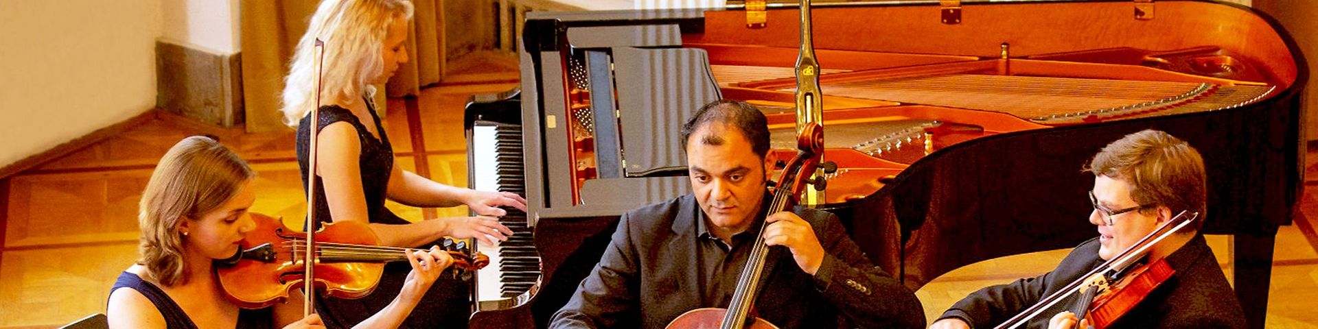 Vier Musiker, eine Frau am Klavier, eine Frau und ein Mann an der Geige, ein Mann am Cello.