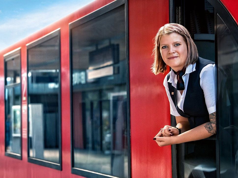 Eine junge Frau schaut aus dem Führerstand eines roten Regionalzuges.