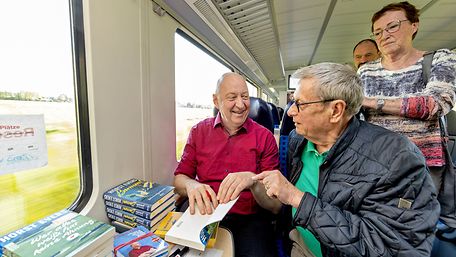 Autor Horst Evers sitzt im Zug, neben im Fans. Er signiert seine Bücher.