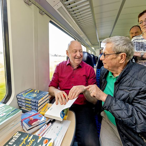 Autor Horst Evers sitzt im Zug, neben im Fans. Er signiert seine Bücher.