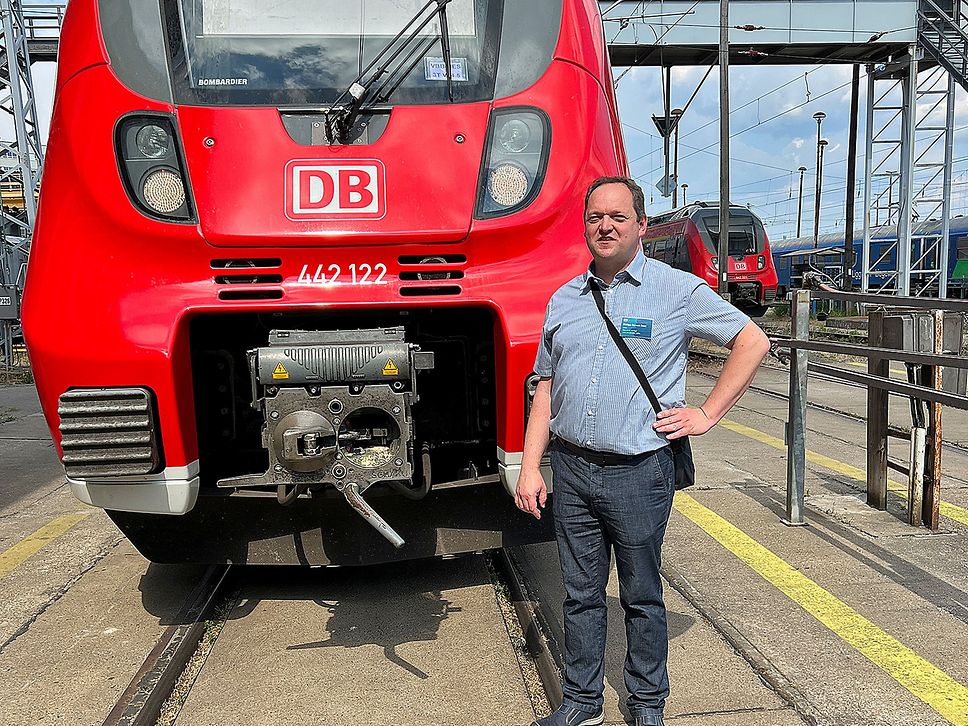 Ein Mann posiert für das Foto vor einem roten Regionalzug.