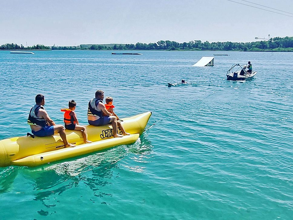 Zwei Erwachsene und zwei Kinder sitzen auf einem gelben Bananenboot und lassen sich über das Wasser ziehen.