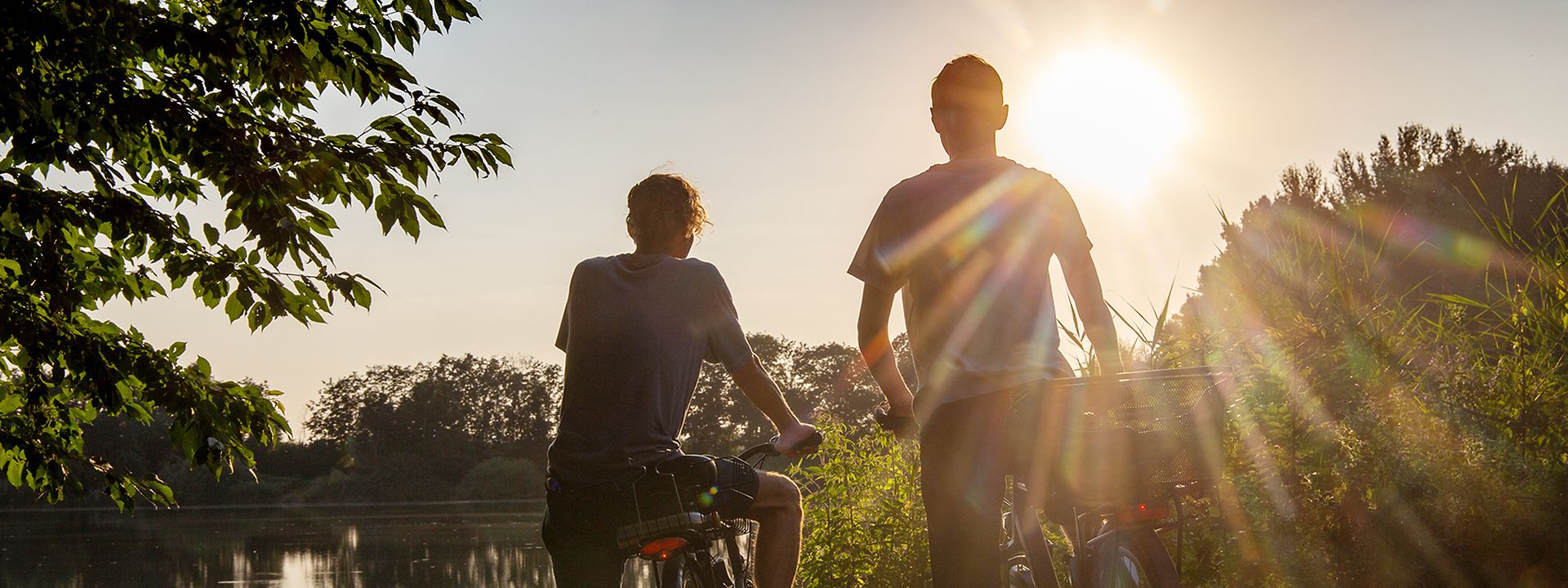 Zwei Fahrradfahrer stehen im Sonnenuntergang an einem See.