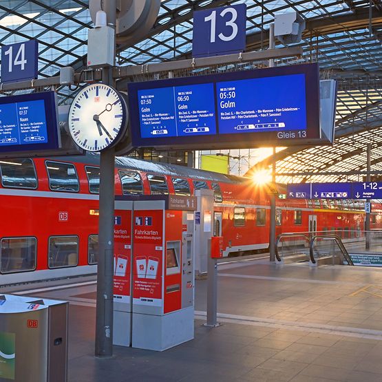 Ein roter Regionalzug steht an einem Bahnsteig, im Hintergrund scheint die Sonne durch das Dach.
