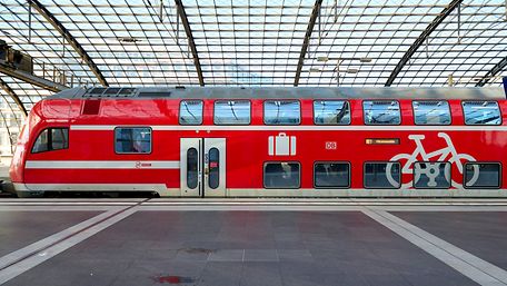 Ein roter Regionalzug steht im Bahnhof an einem Bahnsteig.