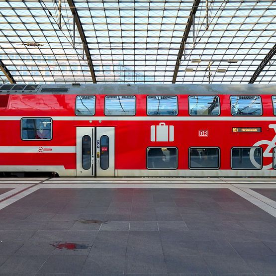 Ein roter Regionalzug steht im Bahnhof an einem Bahnsteig.