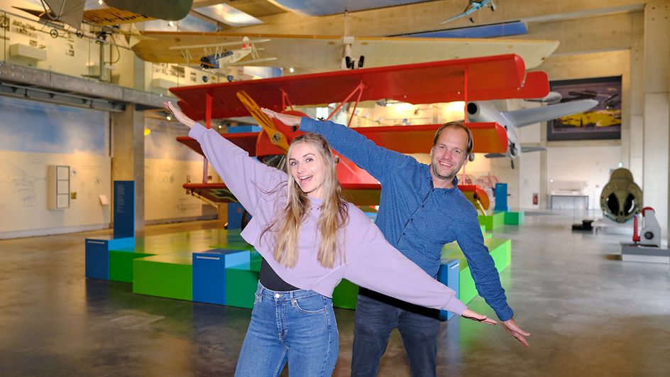 Maike und Olli posieren mit ausgestrecken Armen vor Flugzeugmodellen im Phantechnikum.