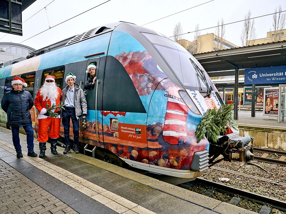 Das Nikolauszug-Team steht vor dem Zug am Bahnsteig und schaut in die Kamera. 
