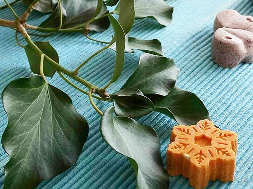 Zwei Badepralinen liegen mit einem Zweig mit grünen Blättern auf einem blauen Tuch.