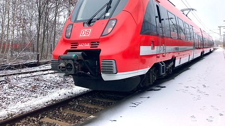 Ein roter Regionalzug auf der Schiene, es liegt etwas Schnee.