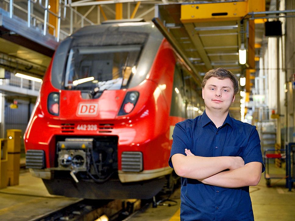 Niklas Osbahr trägt ein blaues Hemd und steht neben einem roten Regionalzug.