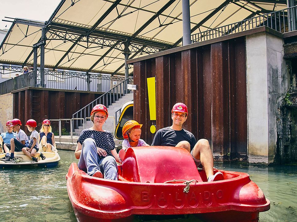 Tretboote auf dem Wasser, im Vordergrund eine Familie in einem roten Boot.