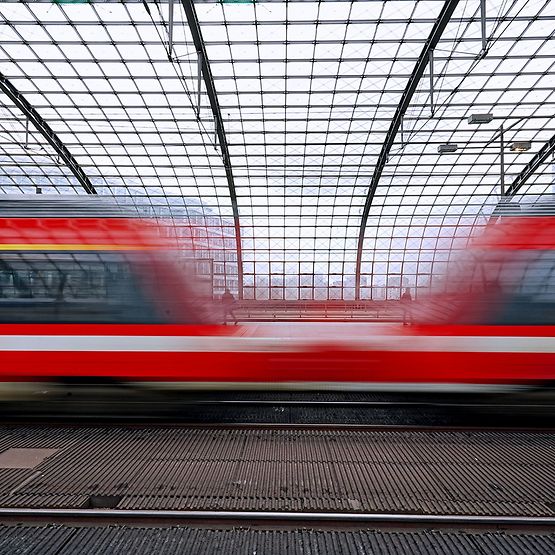 Verschwommene Darstellung zweier roter Regionalzüge, die durch einen Bahnhof fahren.