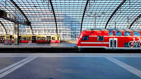 Eine Berliner S-Bahn und ein roter Regionalzug stehen sich am Bahnhof gegenüber.