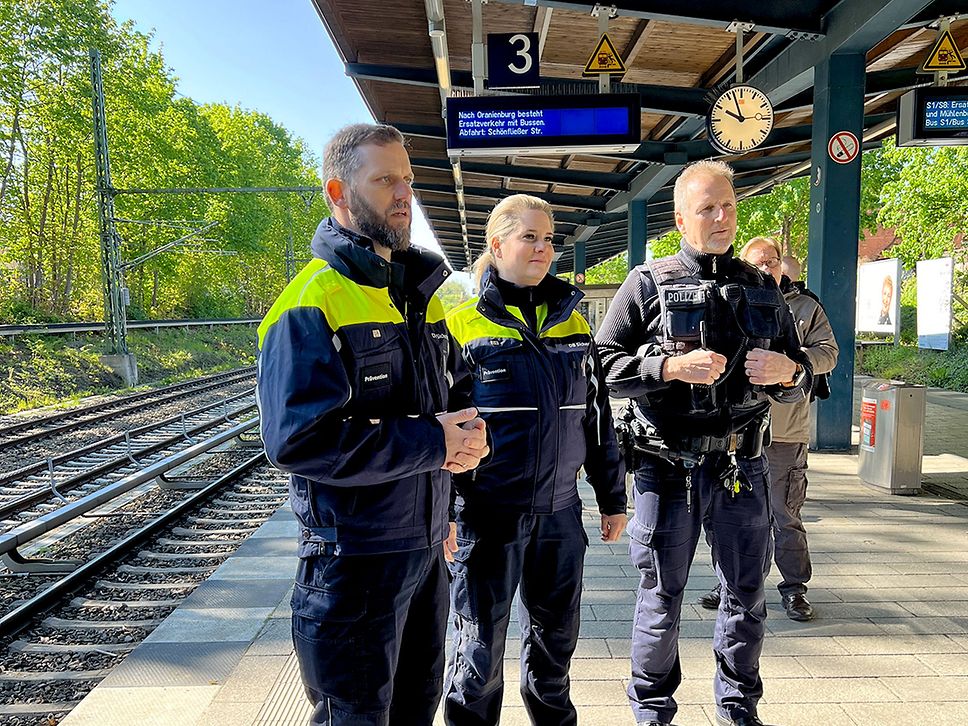 Zwei männliche Polizisten und eine weibliche Kollegin stehen auf einem Bahnsteig.