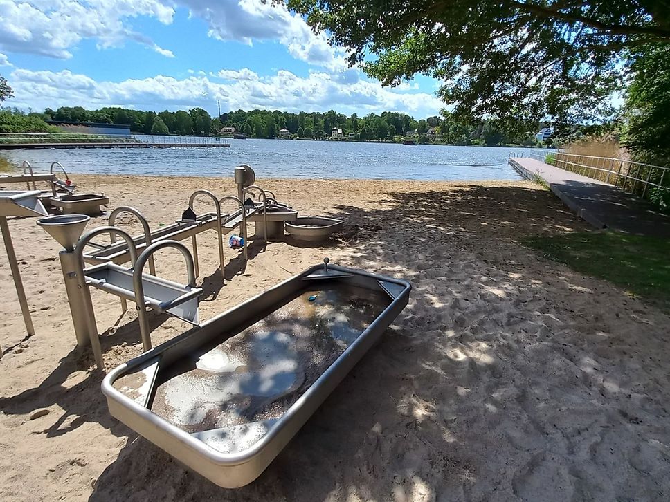Blick auf eine Badestelle, im Vordergrund ein Wasserspielplatz.