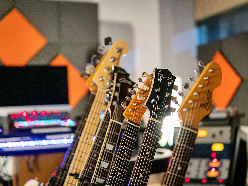Sechs Gitarrenhälse, im Hintergrund ein PC.
