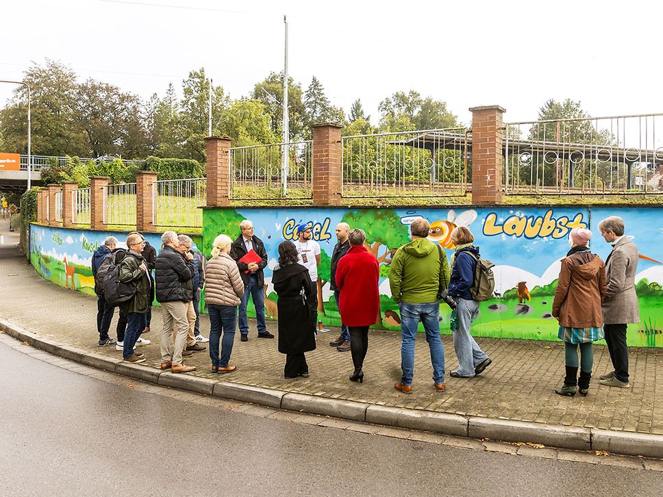 Eine Gruppe Menschen steht auf dem Bürgersteig vor einer Wand mit Graffiti.