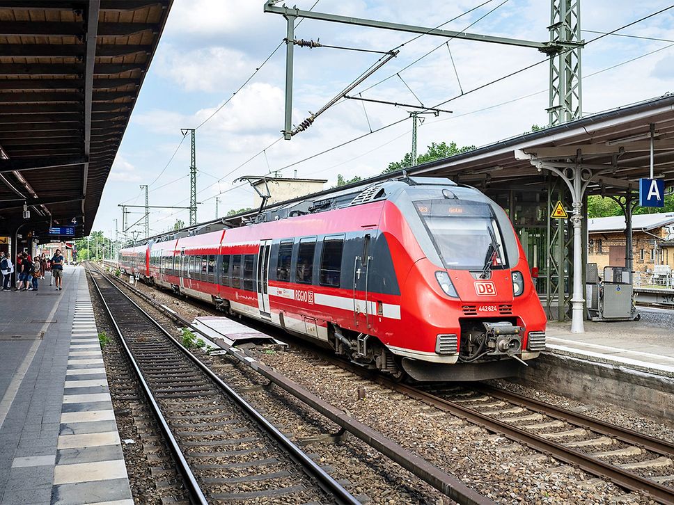 Roter Regionalzug hält an einem Bahnhof.