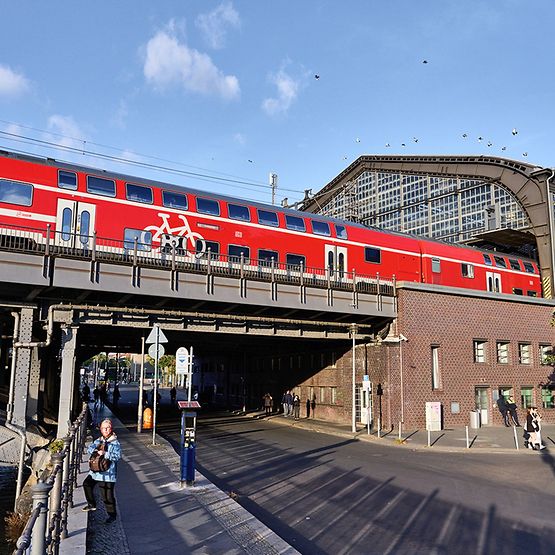 Ein roter Regionalzug fährt über eine Brücke aus einem Bahnhof raus.