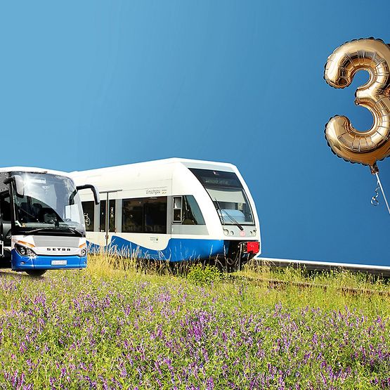 Ein Zug und ein Bus vor blauem Hintergrund, an der Wand eine goldene 30..