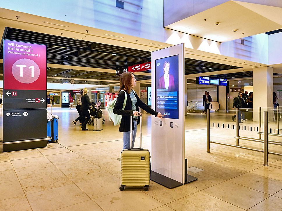 Eine junge Frau steht vor einem Terminal mit Bildschirm und tippt auf das Bedienfeld.