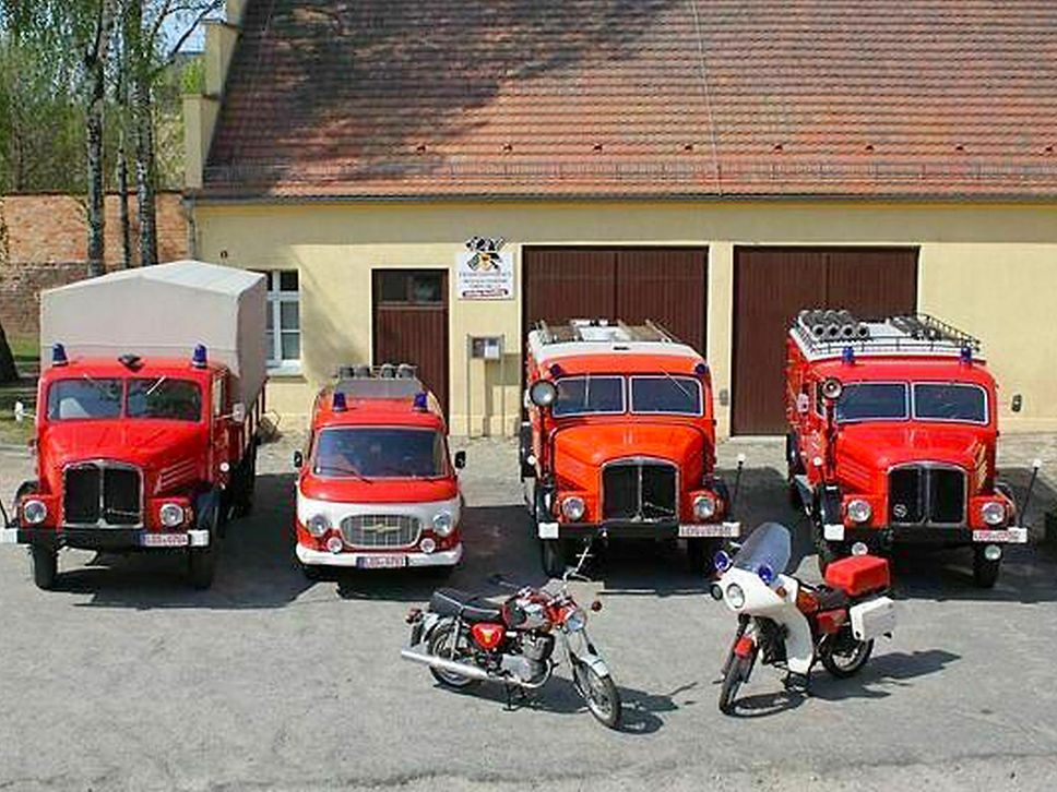 Historische Feuerwehrfahrzeuge stehen vor einem Gebäude.