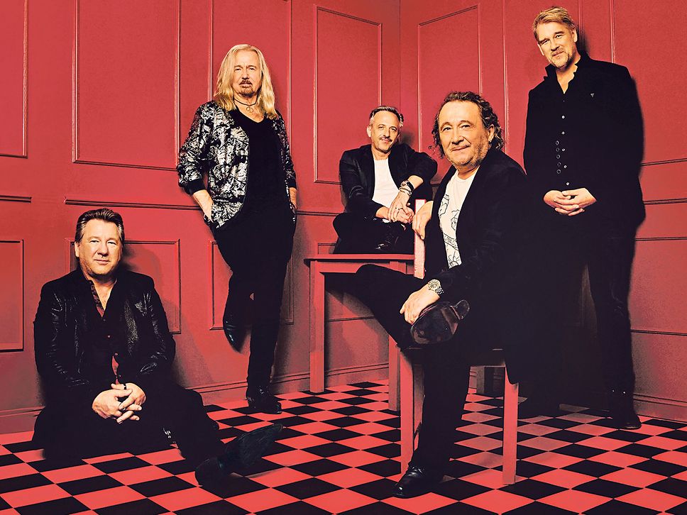Gruppenfoto der fünfköpfigen Band Karat in einem roten Zimmer mit schwarz-rot gekacheltem Fußboden.