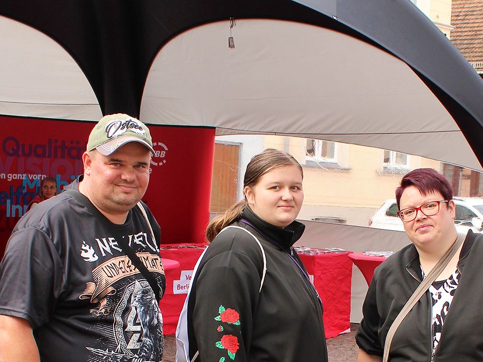 Workshopteilnehmende Marcel, Jasmin und Doreen stehen vor dem Stand und schauen in die Kamera.