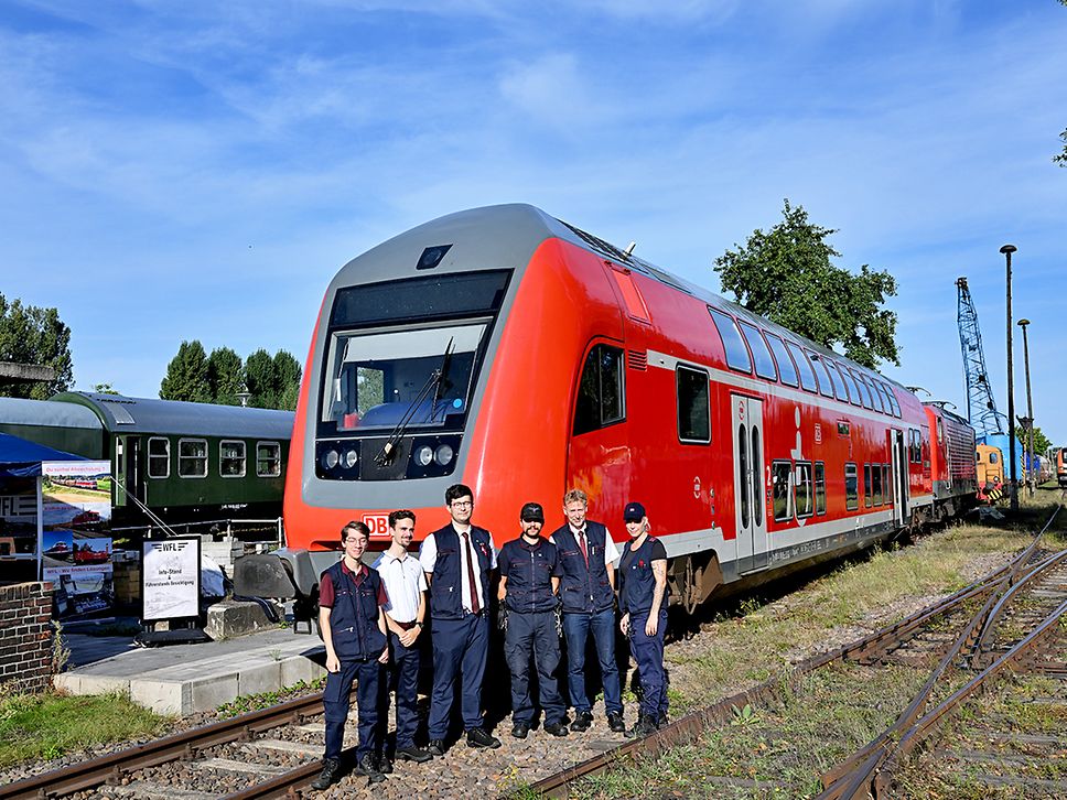 Mitarbeitende in Arbeitskleidung stehen vor einem roten Regionalzug.