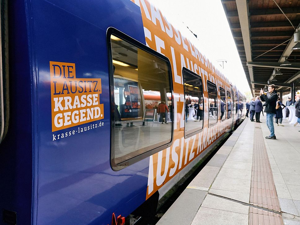 Ein Zug, der Werbung für die Lausitz macht, steht an einem Bahnsteig.