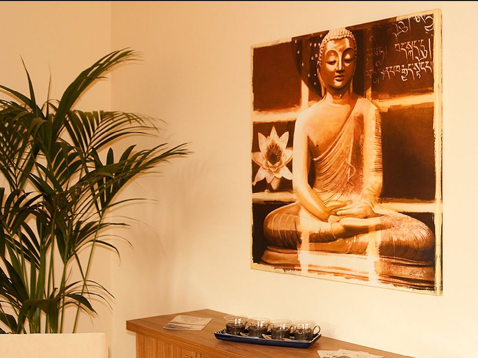 Blick auf ein Wandbild mit sitzendem Buddha, links eine Grünpflanze.