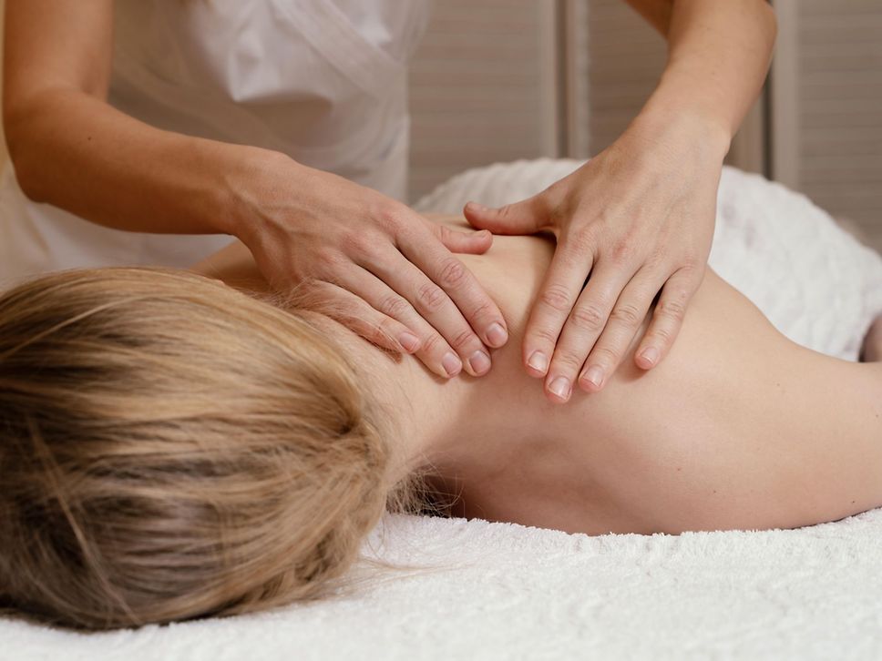 Eine Frau liegt auf dem Bauch und wird an den Schultern massiert.