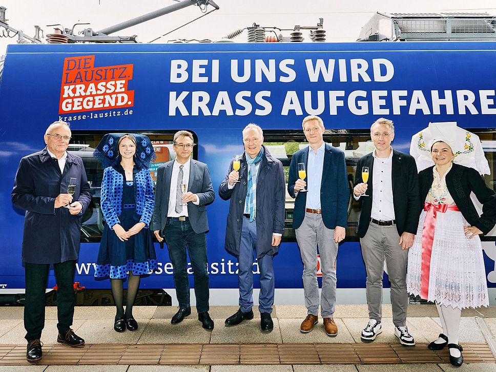 Gruppenfoto vor einem Zug, der für die Lausitz wirbt. Zu sehen sind fünf Männer und zwei Frauen. 