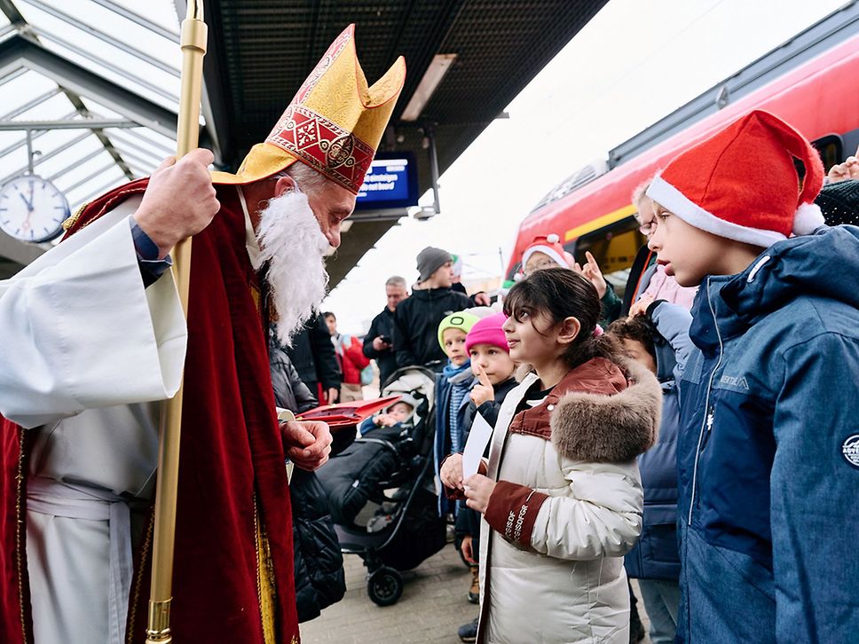 Kinder werden am Bahnhof vom Nikolaus begrüßt.