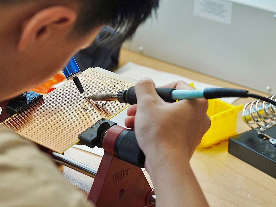 Eine männliche Person lötet etwas auf einer Platte.