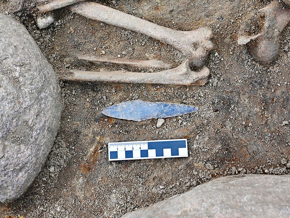 Knochen und ein Stück Metall, das an einen Dolch erinnert, liegen auf dem Boden.