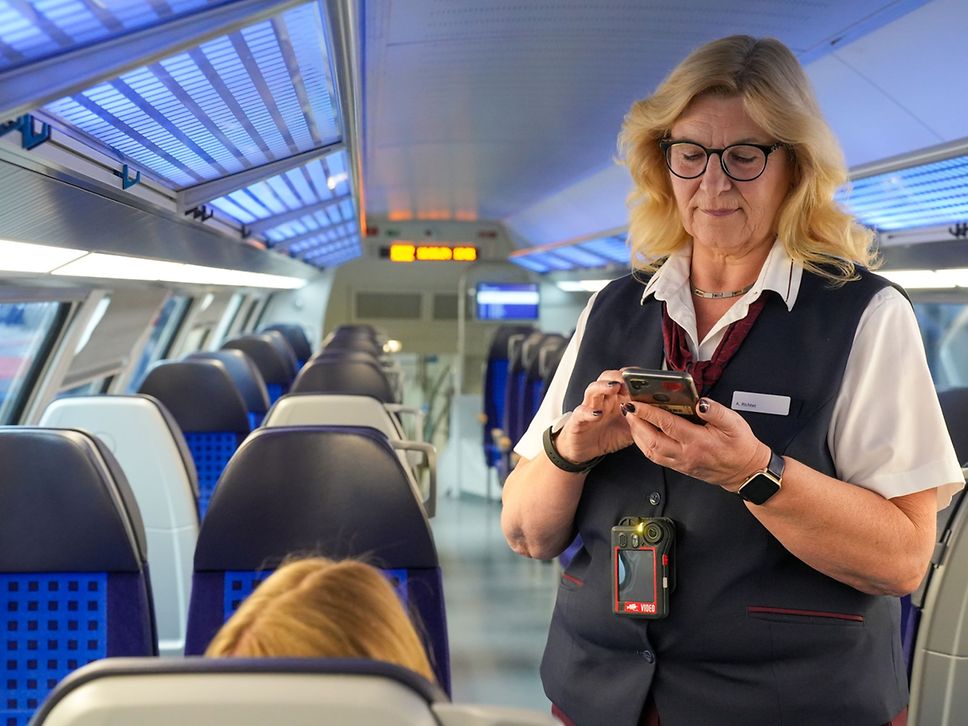 Kundenbetreuerin bei der Fahrkartenkontrolle in einem Regionalzug. Eine Bodycam hängt um ihren Hals.