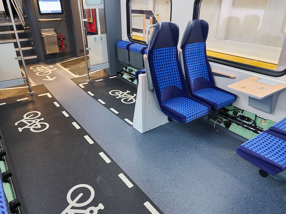 Innenansicht des neuen Fahrzeugs, blaue Sitze, große Fenster und markierte Fahrradstellplätze.