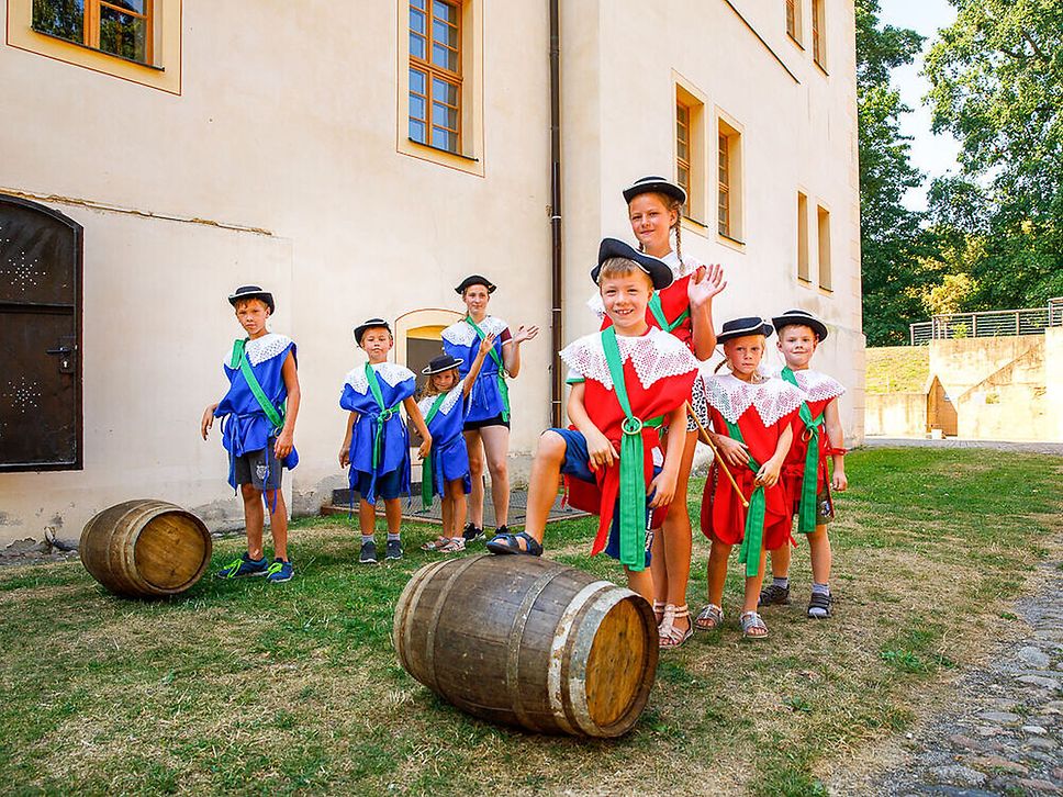 Zwei Kindermannschaften in historischen Kostümen stehen vor Holzfässern und schauen in die Kamera.