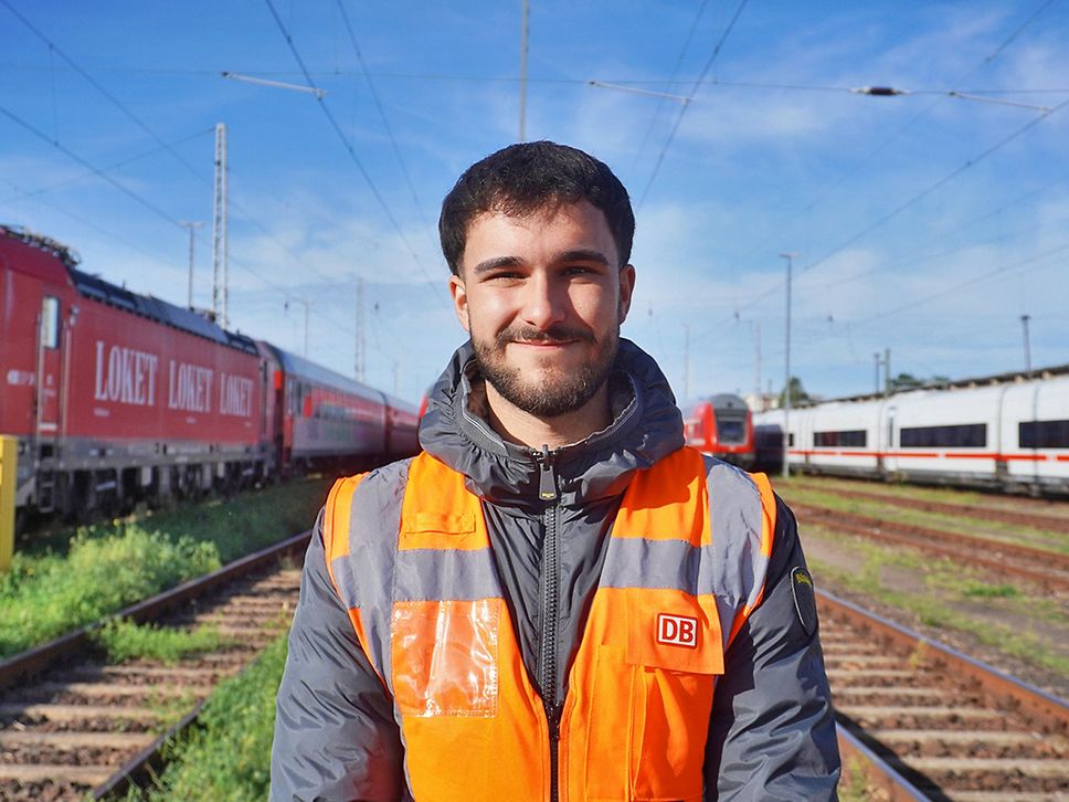 Porträt eines 21-Jährigen Mannes mit kurzen, schwarzen Haare und Bart. Er trägt eine Warnweste.