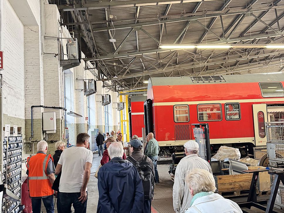 Besucher:innen im Werk Cottbus, im Hintergrund ein Wagen eines roten Regionalzugs.