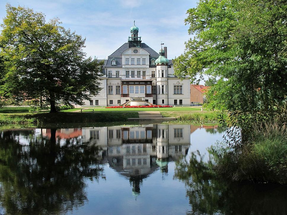 Blick auf ein Schloss mit Park an einem See.