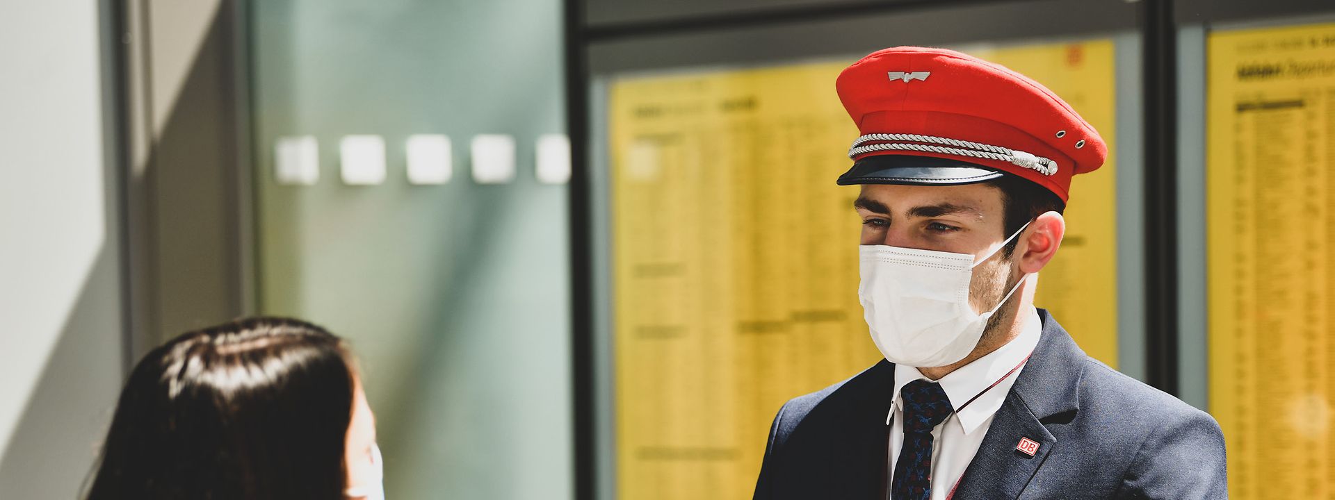 Quelle: DB AG Ein Bahnmitarbeiter berät am Bahnsteig eine Frau zu ihren Verbindungen. Im Hintergrund hängt der Fahrplanaushang.