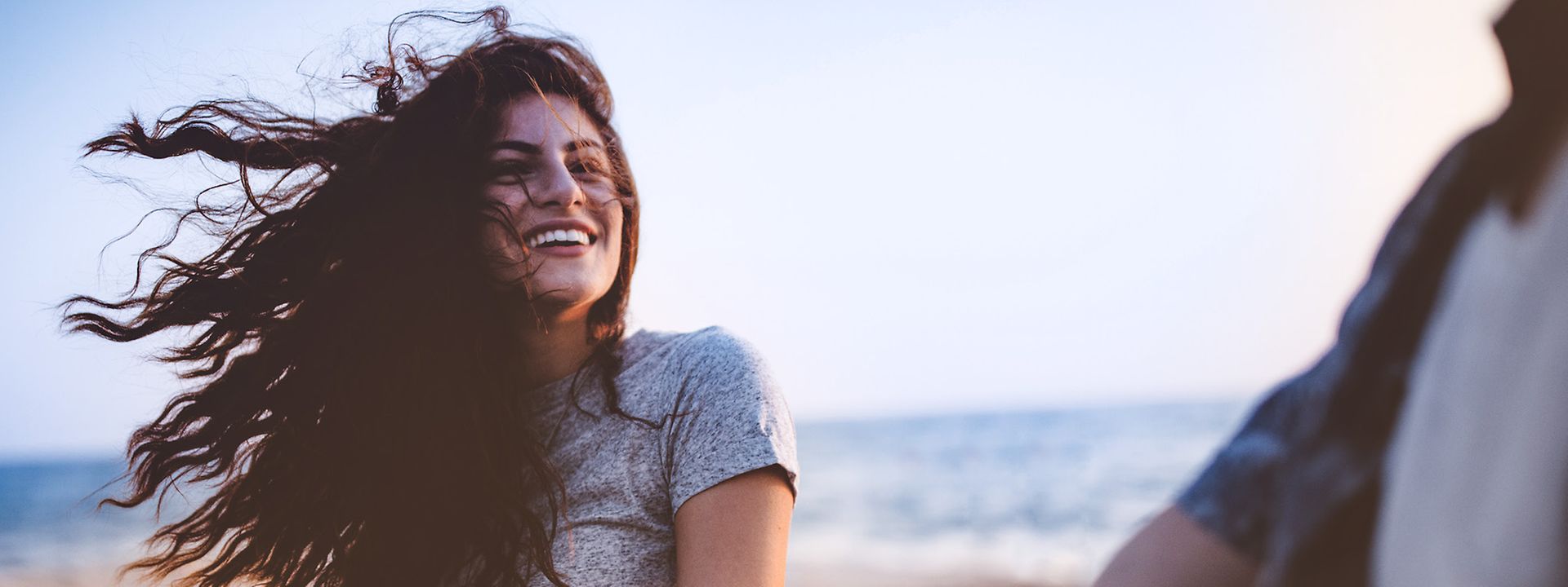 Quelle: DB Regio / istock.com / wundervisuals Junge Frau ist in einer Abendstimmung an einem See unterwegs. Der Wind weht durch ihr langes Haar