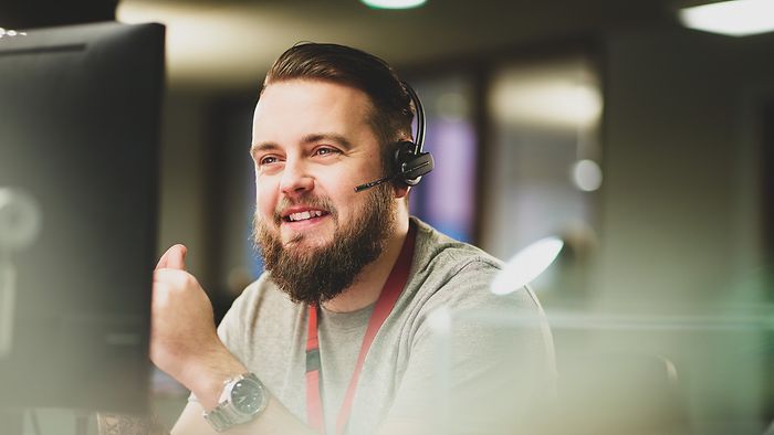 Junger Mann mit Vollbart berät Kunden am Telefon. Er trägt ein Headset.