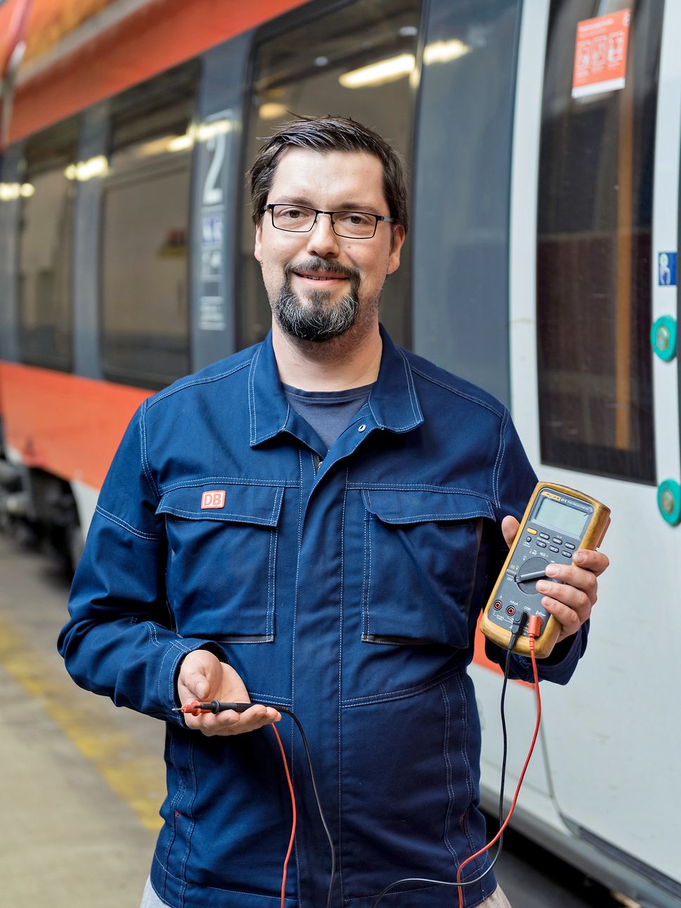 Ein Mann in blauer Arbeitskleidung hat ein Messgerät in der Hand und lächelt in die Kamera.